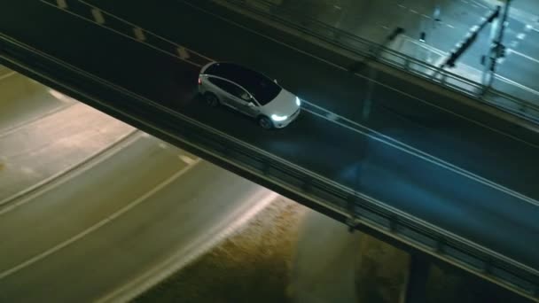 Aerial Drone View of a Modern Luxury White Electric SUV Driving on Urban Highway. Akkumulátoros meghajtású autó halad át üres Bridge Road fényszórókkal éjszaka. Futurisztikus Autonóm Önvezető Autó. — Stock videók