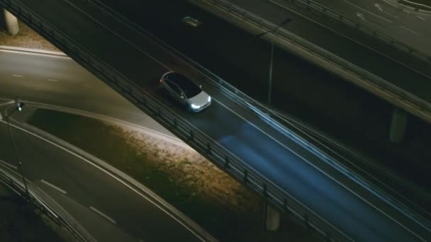 Vista aérea del drone de un SUV eléctrico blanco de lujo moderno que conduce en la carretera urbana. Carro alimentado por batería que se mueve a través de la carretera del puente vacío con faros en la noche. Auto autónomo futurista coche de conducción . — Vídeo de stock