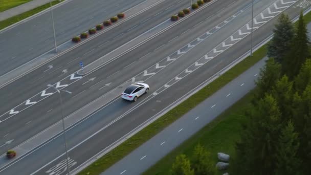 Aerial Drone View of a Modern Luxury White Electric SUV Driving on Urban Junction egy felhős napon. Akkumulátorral hajtott autó belép az autópályára. Futurisztikus Autonóm Önvezető Autó. — Stock videók