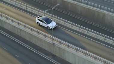 Bulutlu Bir Gün sırasında Şehir Yolu 'nda Modern Lüks Beyaz Elektrikli Geçit Sürüşünün Hava Aracı Görünümü. Pil motorlu araba otobandaki köprüden geçiyor. Panoramik Çatılı Geleceğin SUV 'si.