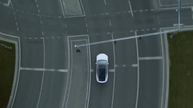 Güneşli bir günde Kentsel Yol 'da Modern Lüks Beyaz Elektrikli Geçit Sürüşünün Hava Aracı Görünümü. Pille çalışan araba trafik ışıklarıyla kavşağa giriyor. Panoramik Çatılı Geleceğin SUV 'si.