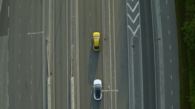 Gündüz vakti Kentsel Yol 'da Günümüz Beyaz Elektrikli SUV' sinin Hava Aracı görüntüsü. Pille çalışan araba şeridi değiştiriyor ve altın renkli lüks bir Sedan 'ı geçiyor. Panoramik Çatı ile Geleceğin Çaprazlaması.
