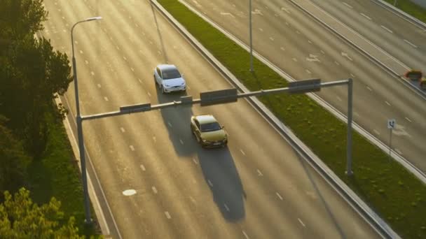 Vista aérea do drone de um SUV elétrico branco moderno que conduz na estrada urbana durante o tempo do dia. Bateria Powered Car Changes Lane e ultrapassa um Sedan de luxo dourado. Crossover futurista com telhado panorâmico . — Vídeo de Stock