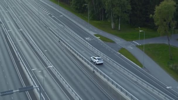 Aerial Drone View of a Modern Luxury White Electric Crossover Jazda na Urban Road podczas Chmury Day. Zasilanie bateryjne zjeżdża z mostu na autostradzie. Futurystyczny SUV z autopilotem. — Wideo stockowe