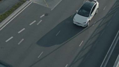 Slow Motion Aerial Drone Modern Lüks Beyaz Elektrikli arazi aracı görüntüsü. Pille çalışan araba, farlar açıkken boş yolda hareket ediyor. Panoramik Çatı ile Geleceğin Çaprazlaması.