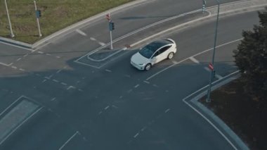 Güneşli bir günde Kentsel Yol 'da Modern Lüks Beyaz Elektrikli Geçit Sürüşünün Hava Aracı Görünümü. Pille çalışan araba trafik ışıklarıyla kavşağa giriyor. Panoramik Çatılı Geleceğin SUV 'si.