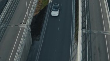 Slow Motion Aerial Drone Modern Lüks Beyaz Elektrikli arazi aracı görüntüsü. Şarjlı araba, viyadikler arasındaki boş yoldan geçiyor. Panoramik Çatı ile Geleceğin Çaprazlaması.