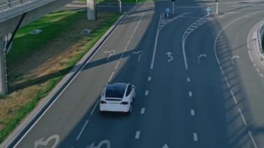 Güneşli bir günde Kentsel Yol 'da Modern Lüks Beyaz Elektrikli Geçit Sürüşünün Hava Aracı Görünümü. Kırmızı Trafik Işığı 'nda pilli araba duruyor. Gelecekçi Otonom Otomatik Sürücü SUV.