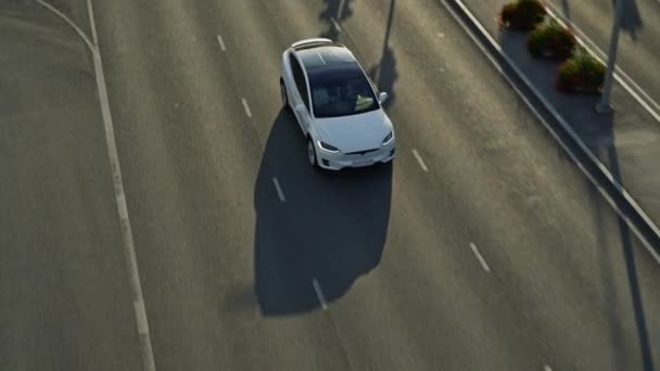 Slow Motion Aerial Drone Ansicht eines modernen weißen Luxus-Elektro-SUV auf der Autobahn. Batteriebetriebenes Auto bewegt sich durch leere lokale Straßen. Futuristischer Crossover mit Panoramadach. — Stockvideo