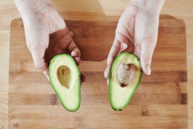 Avokado 'nun iki yarısı elinde çekirdekli bir kesim tahtasının üzerinde.
