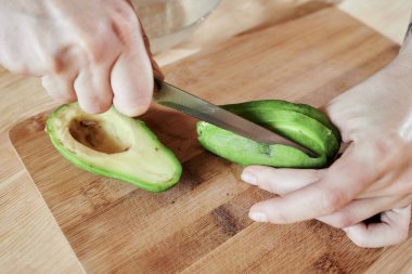 Evin ahşap bir tahtasına kesilmiş bir bıçakla bir avokado kes.