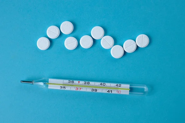 Termómetro corporal con un puñado de pastillas sobre un fondo azul. Vista desde arriba. primer plano — Foto de Stock