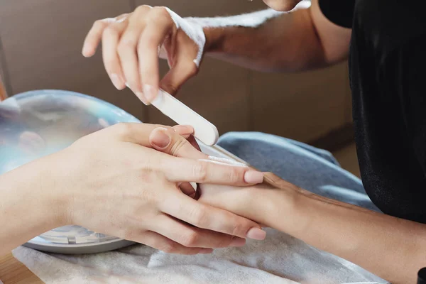 De meester doet een manicure aan de cliënt. zaagt zijn nagels met een schurende grijze zaag. Andere nagels zijn klaar. close-up — Stockfoto