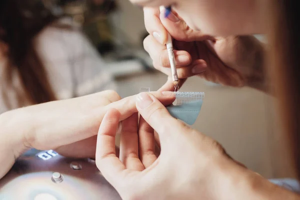 Der Meister überzieht die Nägel des Kunden mit einem Gelpinsel, auf den ein Aufkleber geklebt ist. Nahaufnahme — Stockfoto