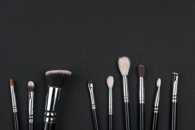 Farklı boyutlarda makyaj fırçaları siyah arka planda yatar. kopyalama alanı.