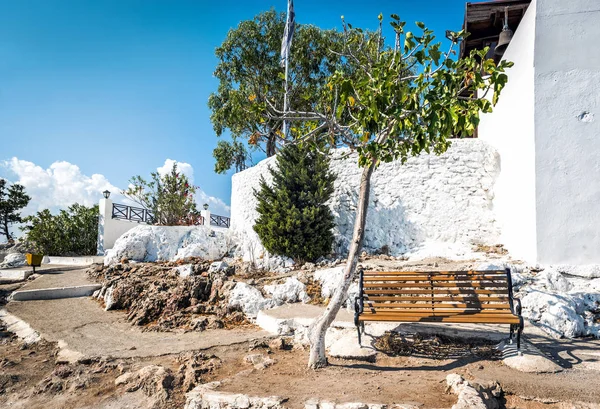 Wooden bench and green tree near walls of Tsampika church at Rhodes island, Greece — Stock Photo, Image