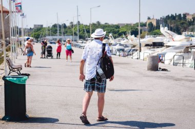 Turist sırt üstünde onun sırt çantası ile deniz bağlantı noktası, Rodos şehir, alan gezinti yolu üzerinde yürüyor. Rodos, Yunanistan  