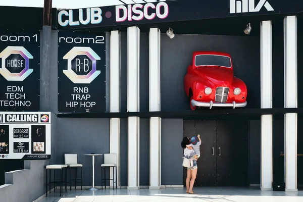 Mujer joven con un niño en sus manos están mirando en un coche, montado en una fachada del club discoteca. Isla de Rodas, Grecia — Foto de Stock