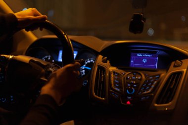 Gece yarısı sürüş, karanlık, kasvetli bir araba, direksiyonda yalnız bir sürücü, sağa keskin bir dönüş, sarı sokak ışığı. Gösterge panelindeki geleneksel radyo fm-ast sembolü, arkadan görünüm