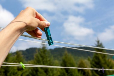 Boş bir kabloya asılmış bir mandal, yeşil eko ormanı doğal açık hava manzarası, bulutlu gökyüzü. Tek bir plastik elbise askısı, kıskaç, çamaşır konsepti, yatay kablolar takmak.