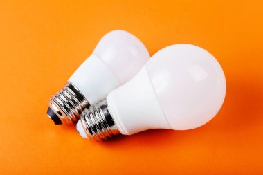 İki küçük parlak beyaz enerji tasarrufu ampulü. Turuncu arka planda izole edilmiş bir çift modern ekolojik ampul. Güç tasarrufu, ekolojik yaşam tarzı, enerji atığı azaltma, elektrik soyut kavramı