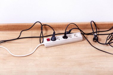 Zeminde kırmızı açma kapama düğmesi olan kablo şeridi, ona bağlı beyaz güç uzatma kablosu prizleri, birbirine dolanmış siyah kablolar, Avrupa tıkaçları, boş oda. Yakın çekim, kopyalama alanı. Elektrik kullanımı kavramı