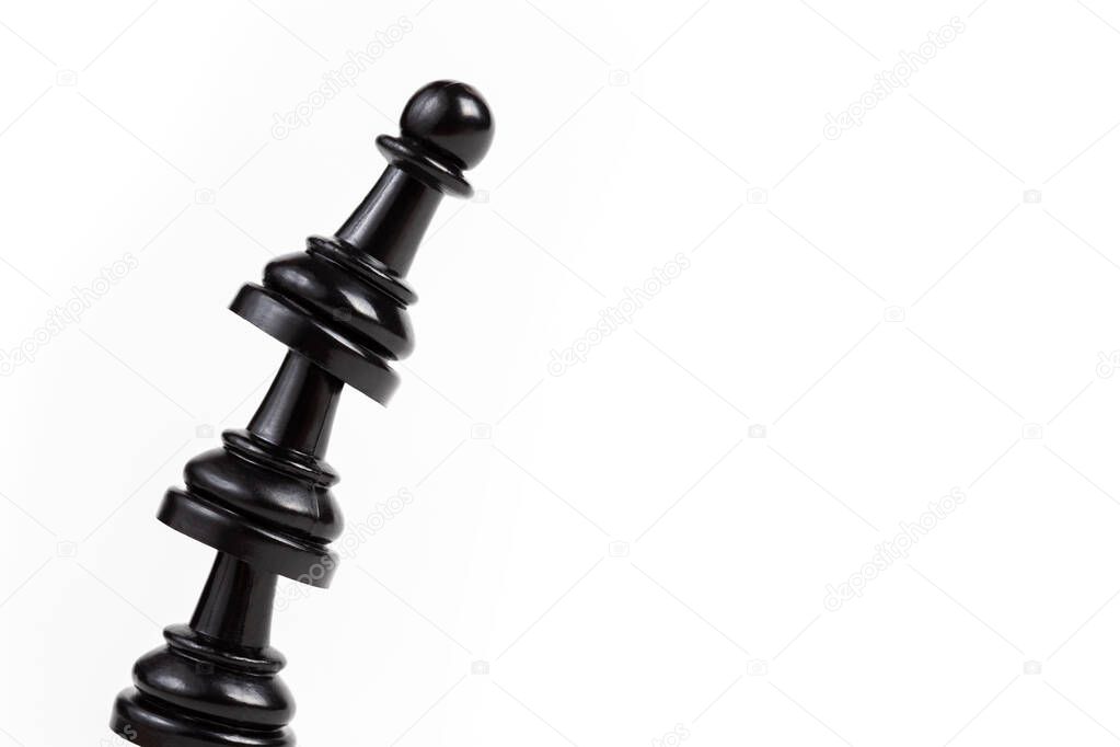 Simple leaning tower made of chess pawn pieces, curved bent construct of black game pieces placed on top of each other. Unstable shaky construction about to fall over / aiming high together concept