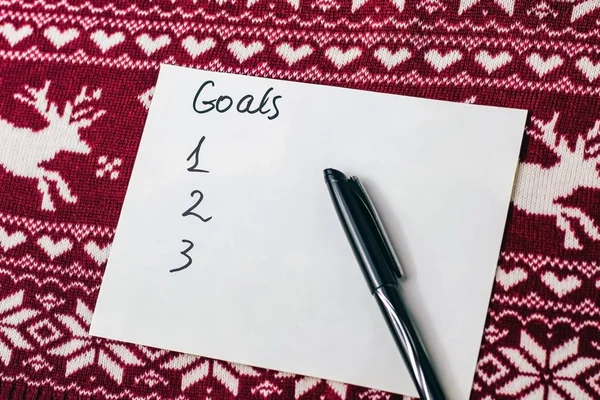 goals written on a sheet with notepad on a background with Christmas symbols