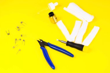 Elektronik sigara ayrıntıları, Vata, bobinler, damlalar, bahar, sarı arka planda meme uçları. yassı yelek