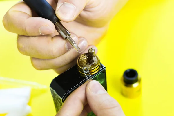 electronic cigarette details, Vata, coils, drip, spring, nippers on a yellow background. man\'s hands change springs in vape
