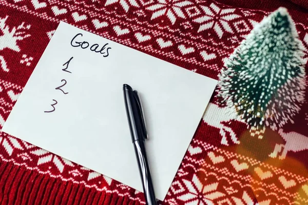 goals written on a sheet with notepad on a background with Christmas symbols