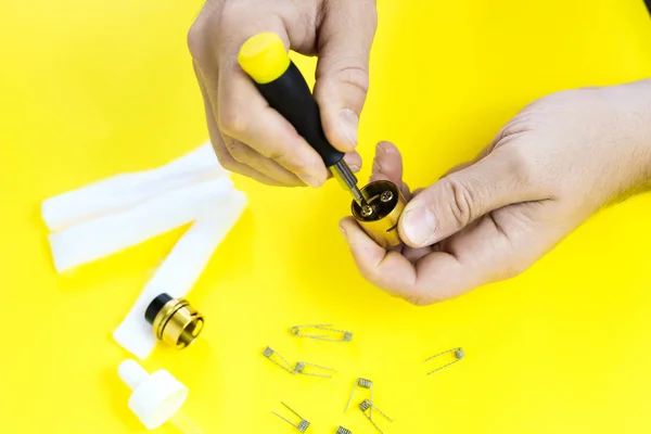 electronic cigarette details, Vata, coils, drip, spring, nippers on a yellow background. man\'s hands take apart vape