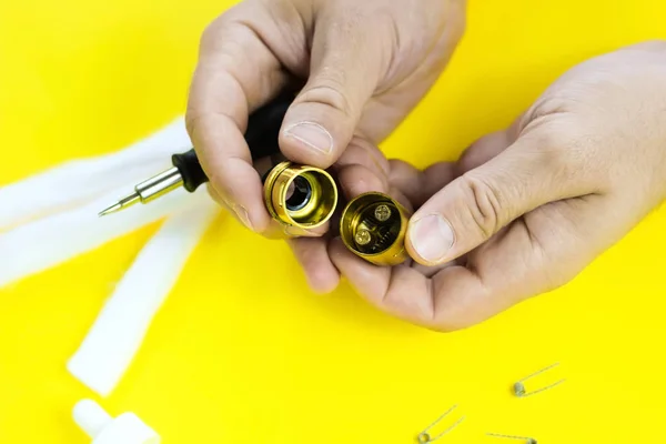 electronic cigarette details, Vata, coils, drip, spring, nippers on a yellow background. man\'s hands take apart vape