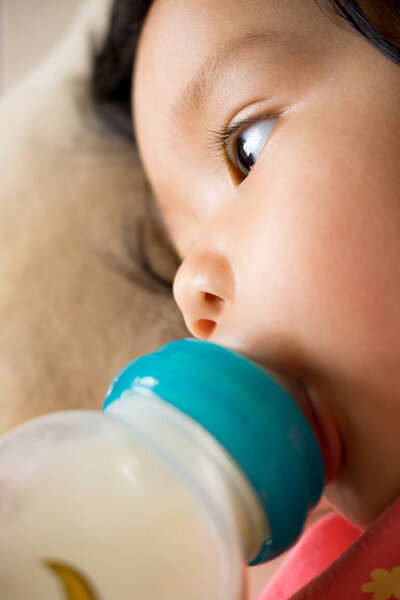 Baby girl is sucking milk from bottle before sleep.