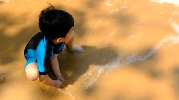 夏天阳光明媚的日子里 一个穿泳衣的男孩坐在沙滩上 在海边玩沙子 — 图库视频影像