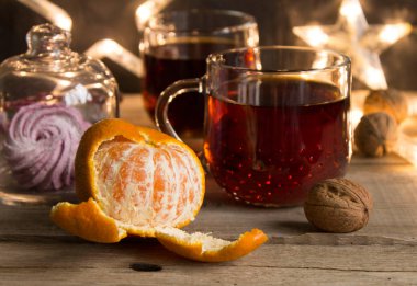 Tahta bir masada cam bir kapsülün içinde tatlı ile kış çay partisi. Bir fincan çay için yıldızlardan, cevizlerden, mandalinadan ve tarçınlı çubuklardan oluşan Noel ışıkları. Noel havası