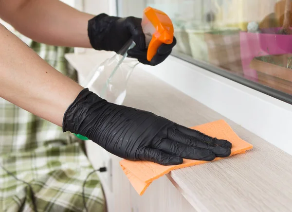 hands in black nitrile gloves wipe the surface of the window sill with detergent and an orange towel