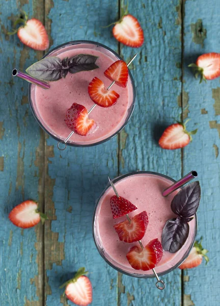 Top view on the strawberry smoothies in a glasses with metal straws, basil leaves, strawberries on cocktail sticks on an old wooden surface