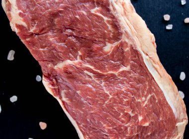 Siyah arka planda pembe tuzlu sulu çiğ biftek.