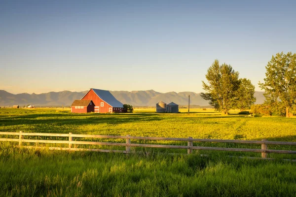 Pôr do sol de verão com um celeiro vermelho em Montana rural e Montanhas Rochosas Imagem De Stock