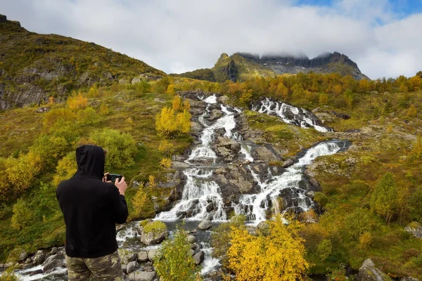 Tourist photographing Lofoten waterfall with a mobile phone in Norway