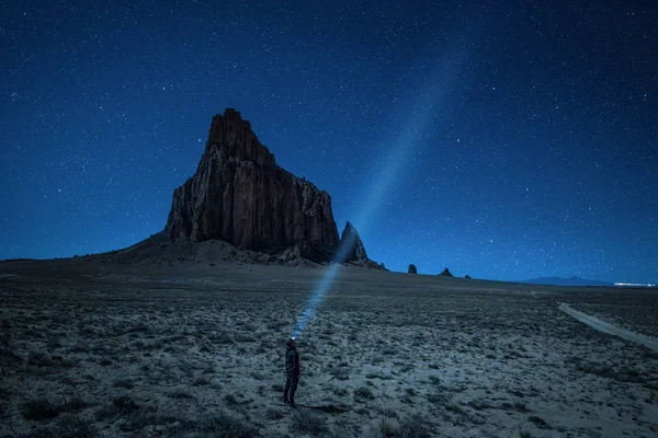 Hiker with a head lamp under the night sky near Shiprock, New Me