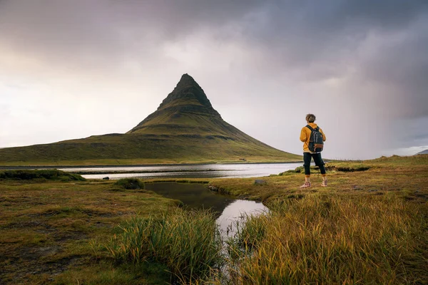 Young hiker with a backpack looks at the Kirkjufell mountain in Iceland — 스톡 사진