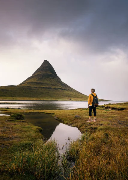 Young hiker with a backpack looks at the Kirkjufell mountain in Iceland — 스톡 사진