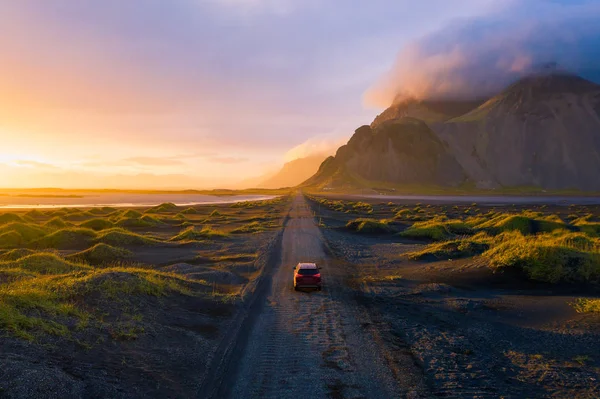 Estrada de cascalho ao pôr do sol com a montanha Vestrahorn e um carro dirigindo, Islândia — Fotografia de Stock