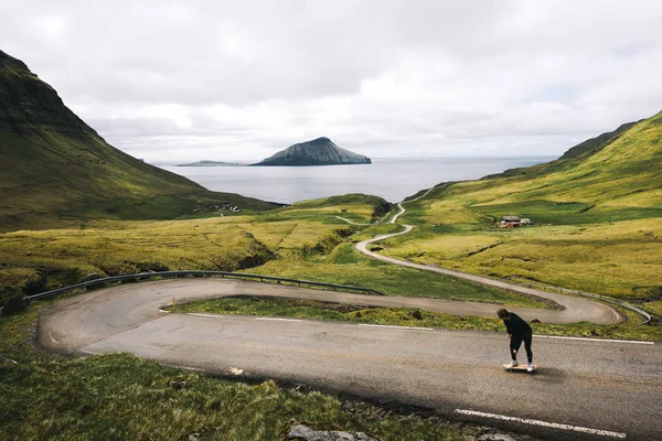 Giovane pattinatore che cavalca uno skateboard attraverso lo splendido scenario delle Isole Faroe — Foto Stock