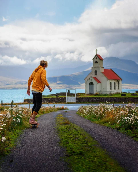 Joven skater skateboarding hacia una iglesia y un cementerio en Islandia — Foto de Stock