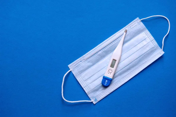 Medical digital thermometer and medical mask on a blue background. Medical banner template with copy space, header layout.