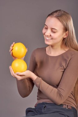 Gri bir arka planda iki portakalla poz veren güzel bir genç kız..