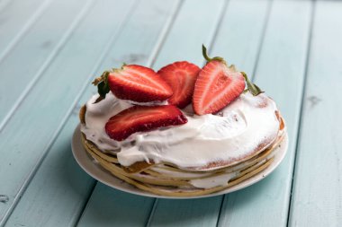 Çilekli krep pastası. Kremalı ve dutlu tatlı. Ulusal mutfak. Tahta masadaki tatlı hamur işleri. Turkuaz tahtaların arkaplanı.